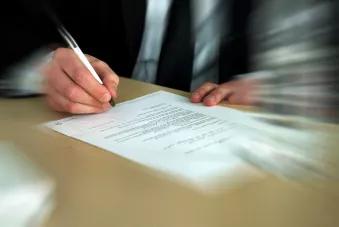 Photo montrant la main d'un homme en train de signer un document écrit sur une feuille blanche