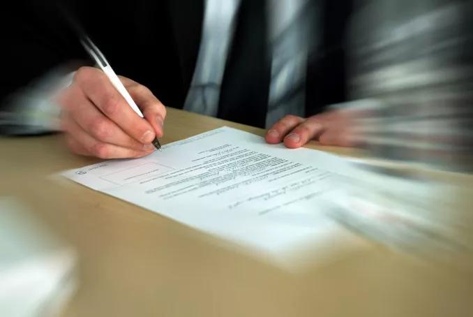 Photo montrant la main d'un homme en train de signer un document écrit sur une feuille blanche