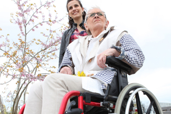 Jeune femme poussant une personne âgée dans un fauteuil roulant, dans un jardin