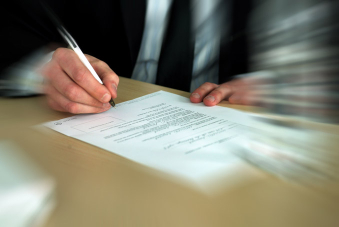 Photo montrant la main d'un homme en train de signer un document écrit sur une feuille blanche