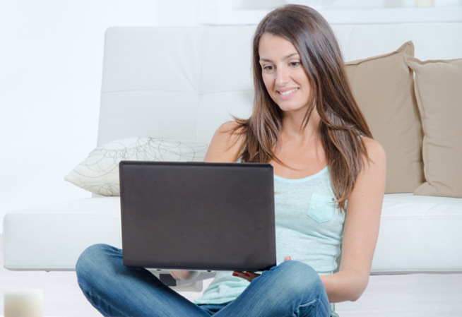 Visuel présentant une femme souriante et assise par terre avec un ordinateur sur le genou