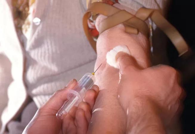 Visuel présentant les mains d'une personne effectuant une prise de sang dans le brad d'un patient