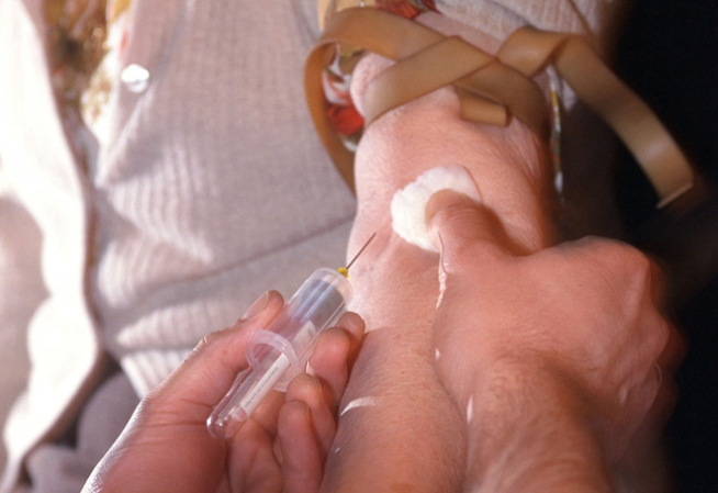 Visuel présentant les mains d'une personne effectuant une prise de sang dans le brad d'un patient