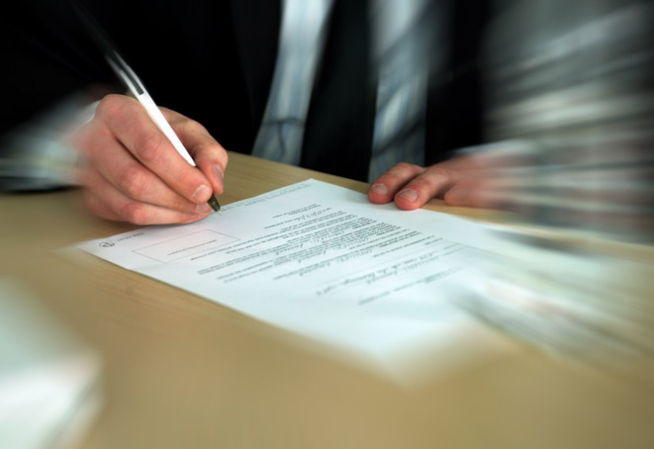 Photo montrant la main d'un homme en train de signer un document écrit sur une feuille blanche