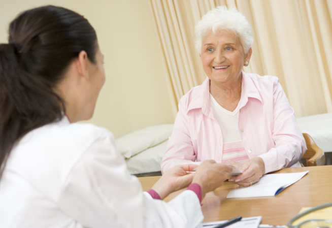 Photo présentant une patiente âgée avec des vêtements clairs en face d'un médecin femme en blouse blanche vue de dos