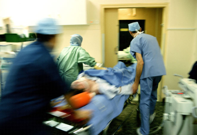 Photo montrant un patient pris en chrage en urgence dans un hôpital et emmené sur un brancard par 3 médecins